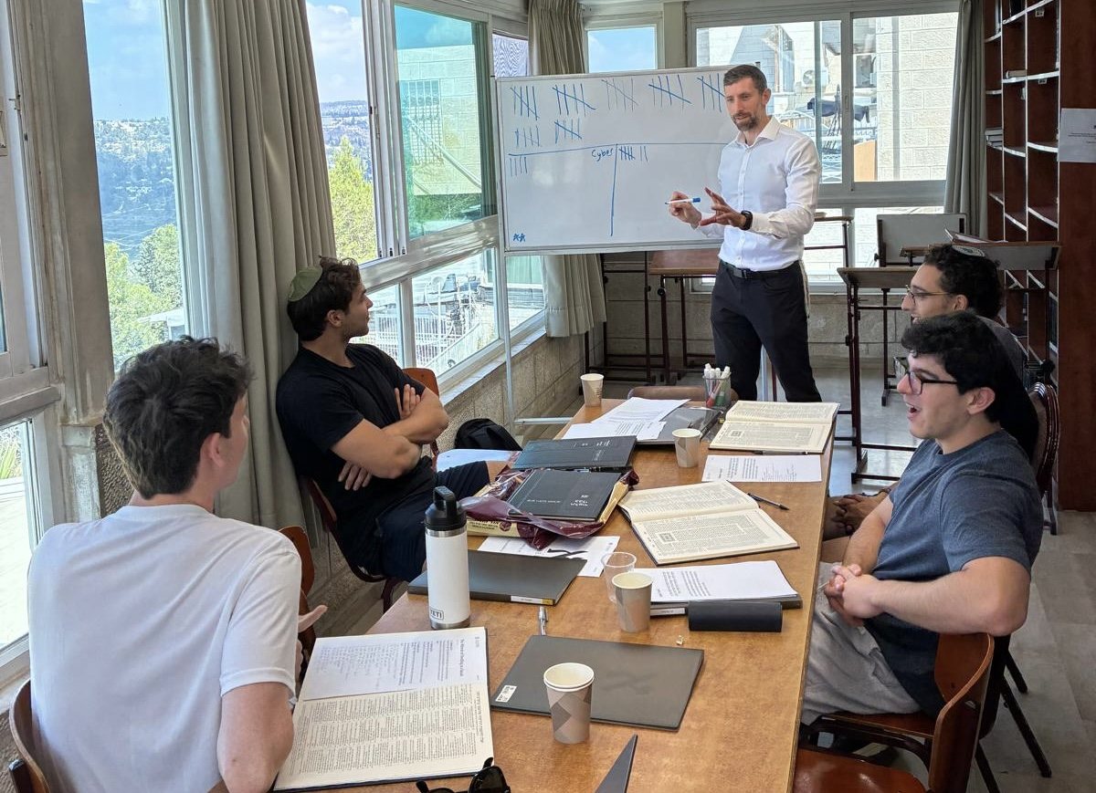 Students learning together around a table with a rabbi at the whiteboard