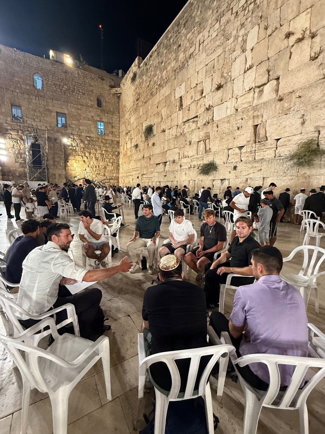 Students learning together in a circle at the Kotel at night